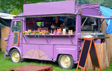 Ein Lila Foodtruck der auf einer Wiese abgestellt ist