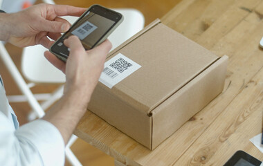 Ein Paket und desen QR Code das auf einem Tisch liegt wird von einer Person mit dem Handy gescannt