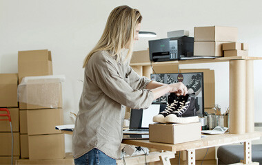 Eine Frau die an einem Schreibtisch Ihre Schuhe in einem Versandkartons verpackt