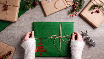 Ein grünes Geschenk das von zwei Händen auf einen Tisch gelegt wird